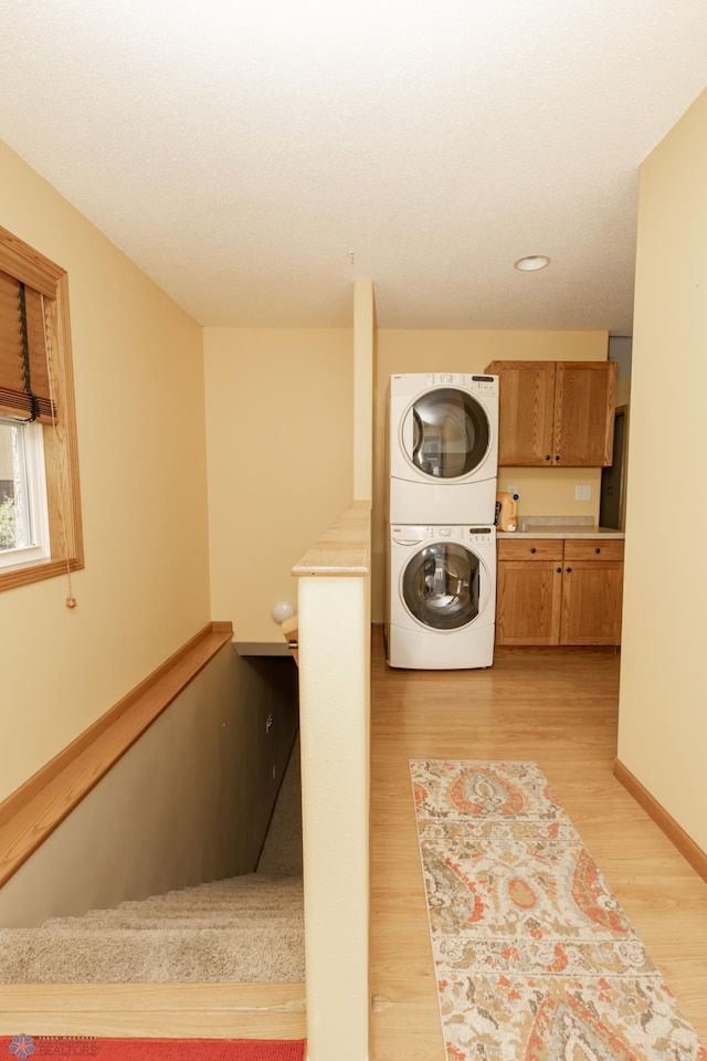 clothes washing area with stacked washing machine and dryer, light wood-style floors, and baseboards