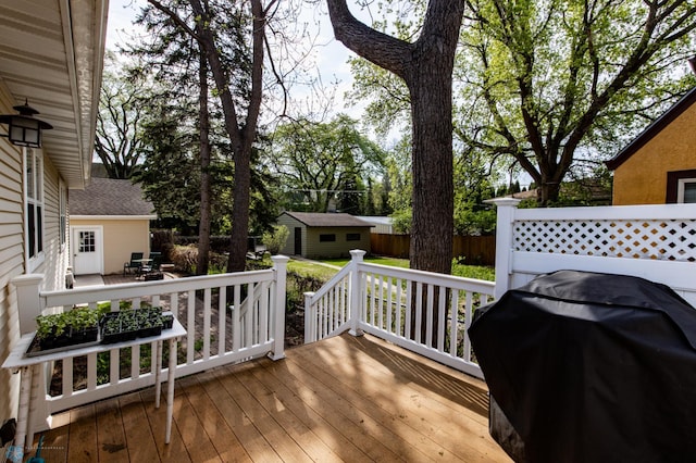 wooden terrace featuring an outbuilding, a grill, and fence