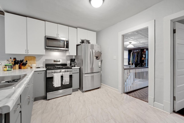1925 Glenwood Ave, Minneapolis, MN 55405 - kitchen featuring appliances with stainless steel finishes, baseboards, a sink, white cabinetry, and light marble finish flooring