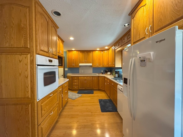 kitchen with white appliances, a textured ceiling, light wood-type flooring, brown cabinets, and light countertops