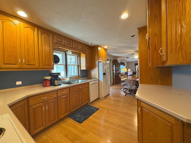kitchen featuring white appliances, a sink, brown cabinetry, a textured ceiling, and light wood-type flooring