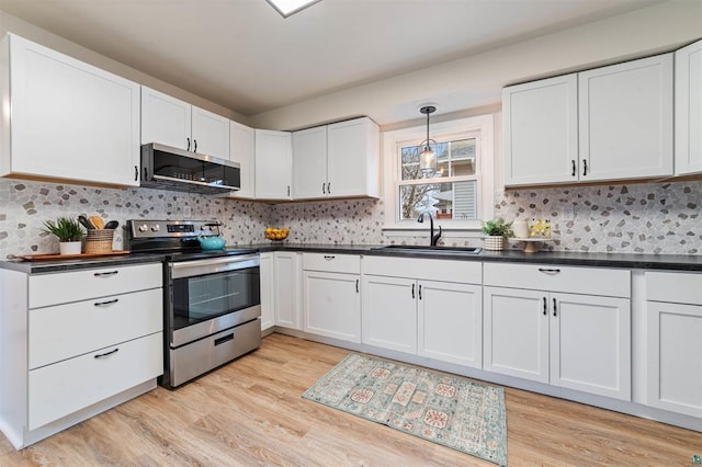 kitchen with a sink, stainless steel appliances, dark countertops, and light wood-style floors