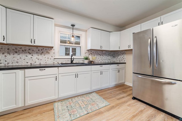 kitchen with freestanding refrigerator, dark countertops, light wood-type flooring, and a sink