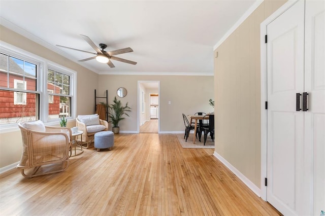 sitting room featuring light wood finished floors, ornamental molding, baseboards, and ceiling fan