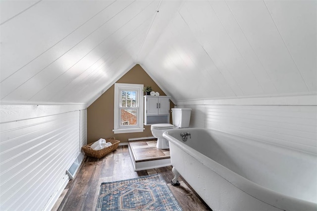 bathroom with lofted ceiling, toilet, a tub to relax in, wood walls, and wood finished floors