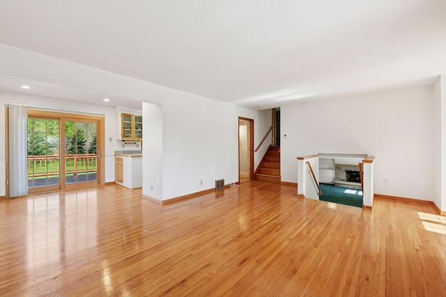 unfurnished living room featuring recessed lighting, a fireplace with raised hearth, visible vents, stairs, and light wood-type flooring