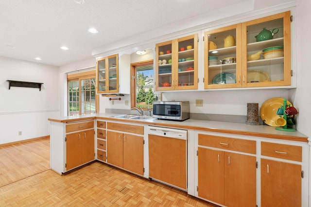 kitchen featuring stainless steel microwave, a peninsula, a sink, dishwasher, and light countertops