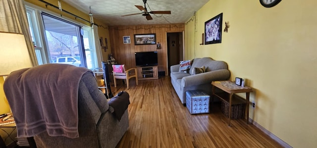 living room featuring wood finished floors, a ceiling fan, baseboards, and wooden walls