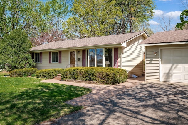 ranch-style house featuring an attached garage, a shingled roof, a front lawn, and aphalt driveway