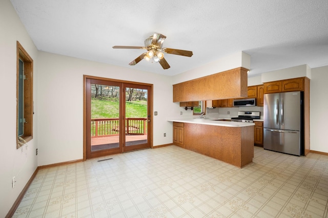kitchen with brown cabinetry, baseboards, a peninsula, light countertops, and appliances with stainless steel finishes