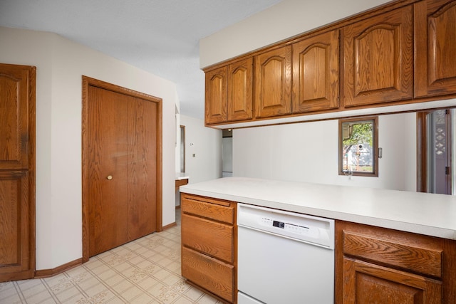 kitchen featuring white dishwasher, light floors, brown cabinetry, baseboards, and light countertops