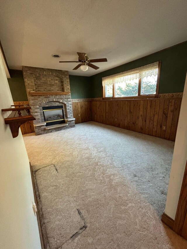 409 4th St NE, Hayfield, MN 55940 - unfurnished living room featuring carpet floors, wainscoting, wood walls, a ceiling fan, and a fireplace