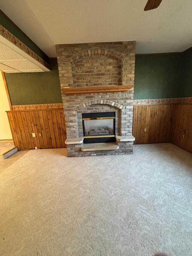 409 4th St NE, Hayfield, MN 55940 - unfurnished living room with wooden walls, carpet flooring, wainscoting, a brick fireplace, and ceiling fan