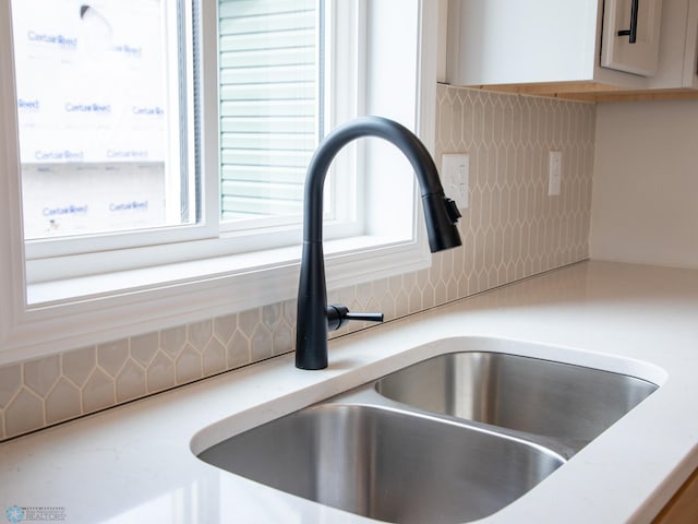 room details featuring white cabinetry, decorative backsplash, and a sink
