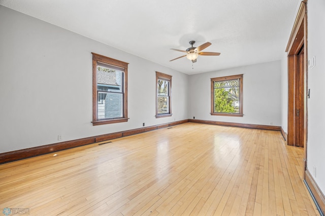 spare room featuring a ceiling fan, plenty of natural light, baseboards, and light wood finished floors