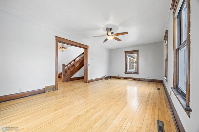 spare room with stairs, a ceiling fan, light wood-style floors, and baseboards