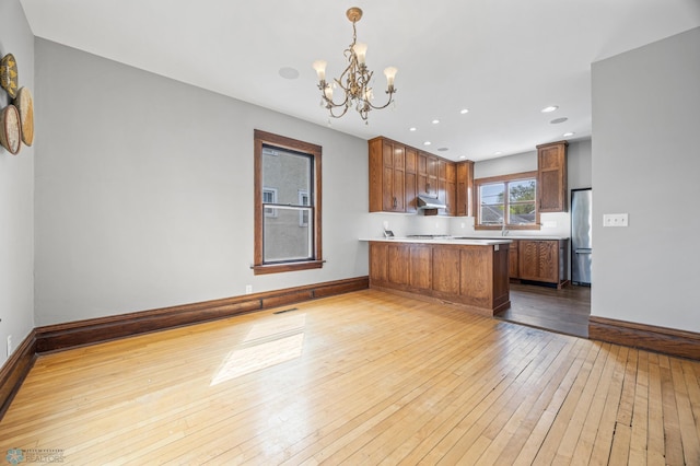 kitchen featuring freestanding refrigerator, light wood-type flooring, a chandelier, a peninsula, and light countertops