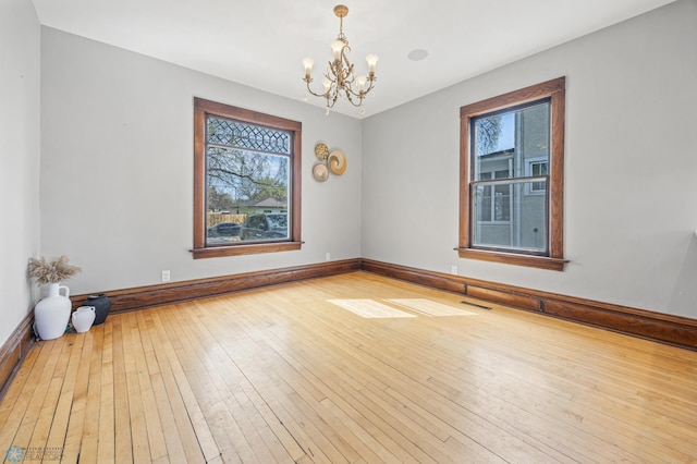 unfurnished room featuring plenty of natural light, a chandelier, wood-type flooring, and baseboards