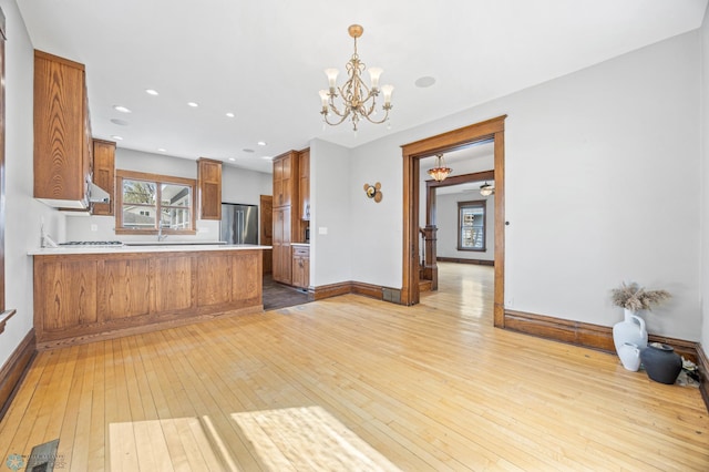 kitchen with high end fridge, light wood-style flooring, brown cabinetry, a chandelier, and a peninsula