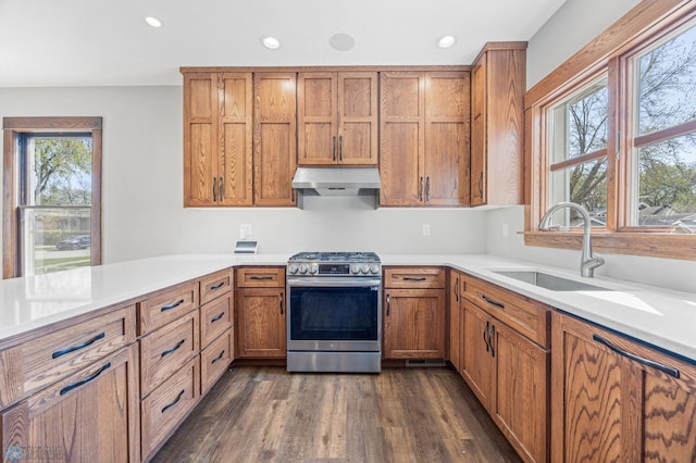 kitchen featuring gas range, a sink, under cabinet range hood, brown cabinetry, and recessed lighting