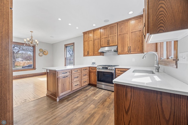 kitchen with stainless steel gas range, a sink, under cabinet range hood, a peninsula, and dark wood-style flooring