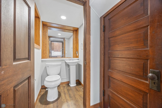 bathroom with toilet, baseboards, wood finished floors, and a sink