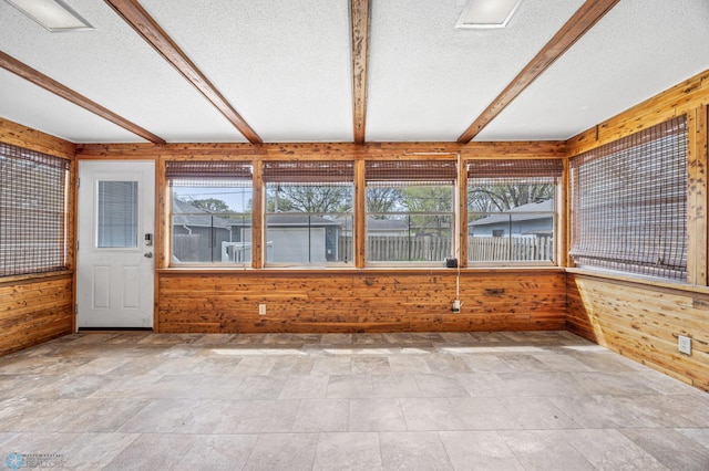 unfurnished sunroom featuring wood walls, beamed ceiling, a textured ceiling, and healthy amount of natural light
