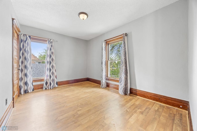 empty room with plenty of natural light, wood finished floors, baseboards, and a textured ceiling