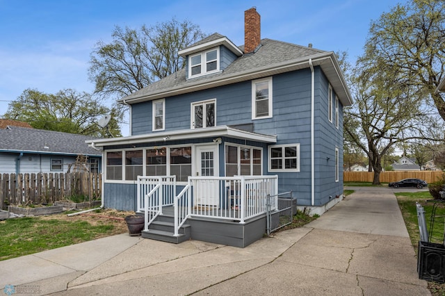 rear view of house with a sunroom, a chimney, fence, driveway, and roof with shingles