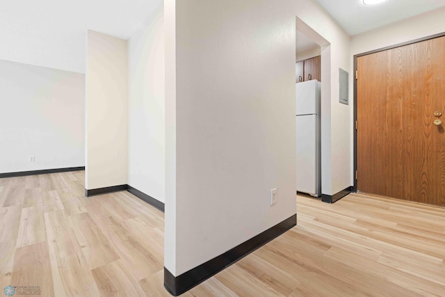 corridor with light wood finished floors, baseboards, and electric panel