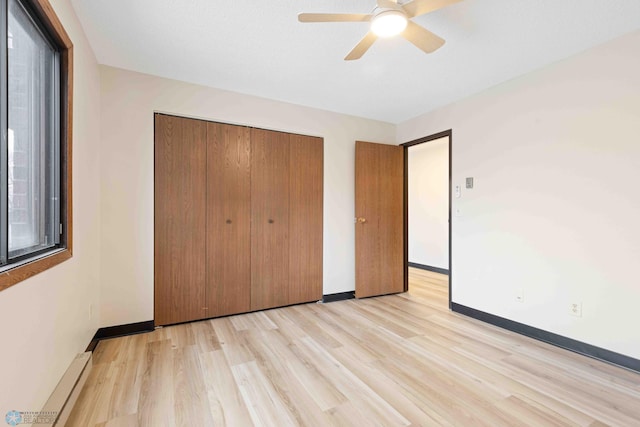 unfurnished bedroom with light wood-type flooring, baseboard heating, baseboards, a closet, and ceiling fan