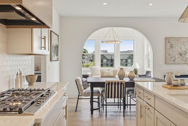 4612 Meadowview Ln, Minnetrista, MN 55331 - kitchen with wall chimney range hood, stainless steel gas stovetop, open floor plan, light stone countertops, and light wood finished floors