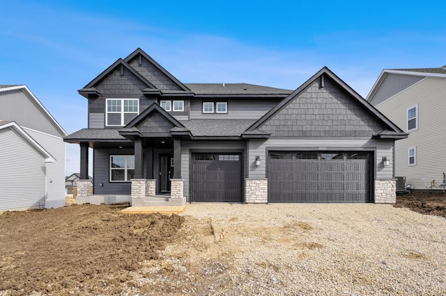 20092 67th Ave, Corcoran, MN 55340 - craftsman-style house featuring an attached garage, a shingled roof, driveway, central AC unit, and stone siding