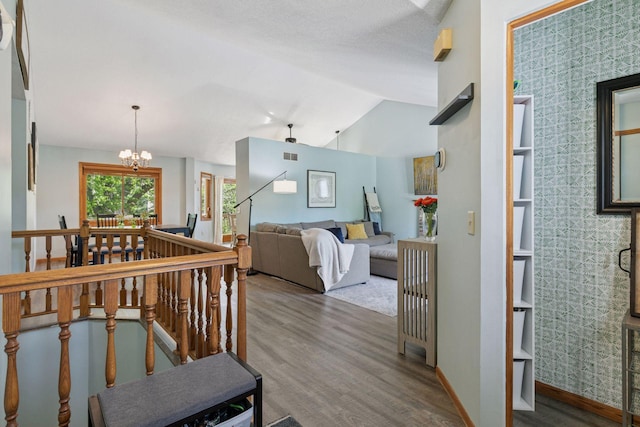 hallway featuring wood finished floors, an upstairs landing, baseboards, a chandelier, and vaulted ceiling
