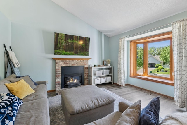 living room featuring wood finished floors, a brick fireplace, vaulted ceiling, and baseboards