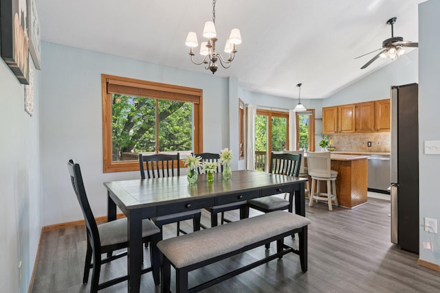 dining space featuring wood finished floors, a ceiling fan, a chandelier, vaulted ceiling, and baseboards