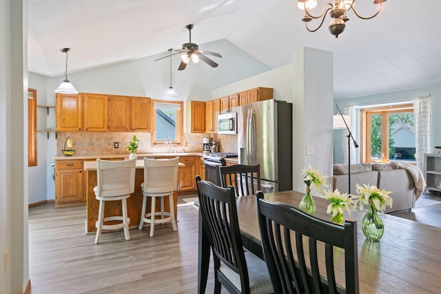 dining space featuring a ceiling fan, healthy amount of natural light, light wood-type flooring, vaulted ceiling, and a chandelier