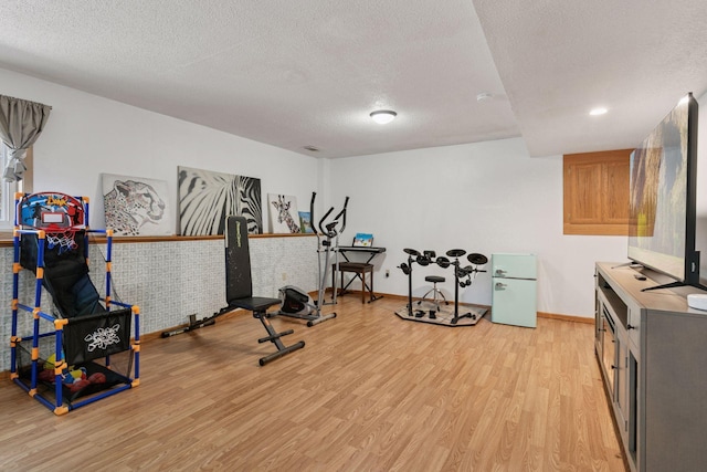 exercise area featuring light wood finished floors, a textured ceiling, and baseboards