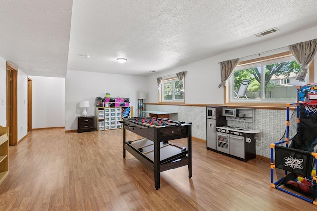 rec room with a textured ceiling, light wood-style flooring, and baseboards