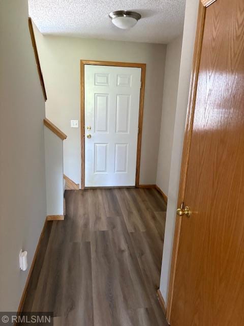 doorway featuring a textured ceiling, wood finished floors, and baseboards