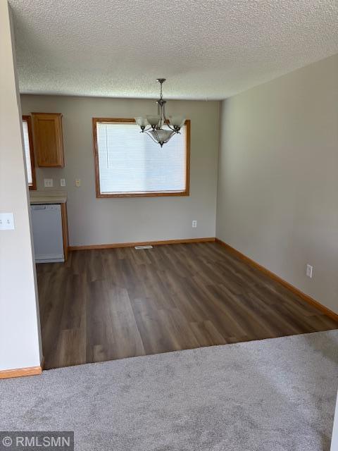unfurnished dining area with a chandelier, dark wood finished floors, baseboards, and a textured ceiling