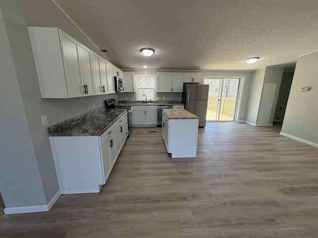 kitchen with appliances with stainless steel finishes, a textured ceiling, a sink, baseboards, and light wood-type flooring