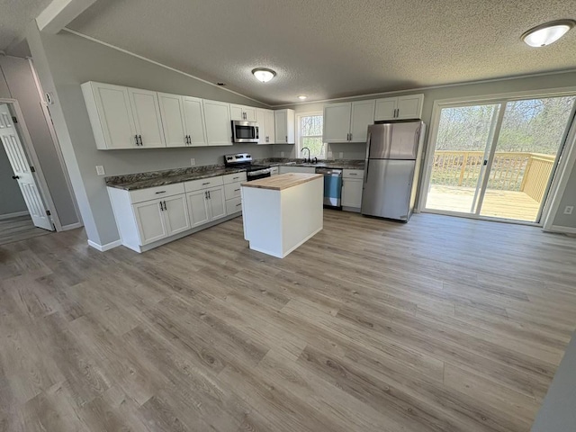 kitchen with stainless steel appliances, a textured ceiling, lofted ceiling, white cabinetry, and wooden counters