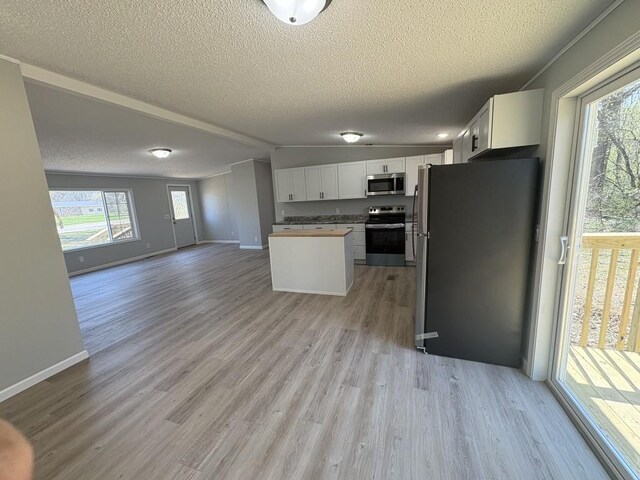 kitchen with stainless steel appliances, open floor plan, a textured ceiling, light wood-type flooring, and white cabinets
