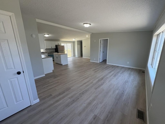 unfurnished living room with a textured ceiling, wood finished floors, and baseboards