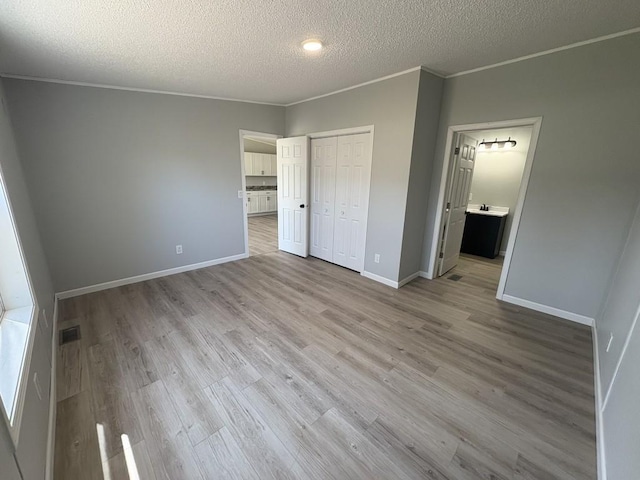 unfurnished bedroom featuring light wood-style floors, a textured ceiling, ornamental molding, baseboards, and connected bathroom