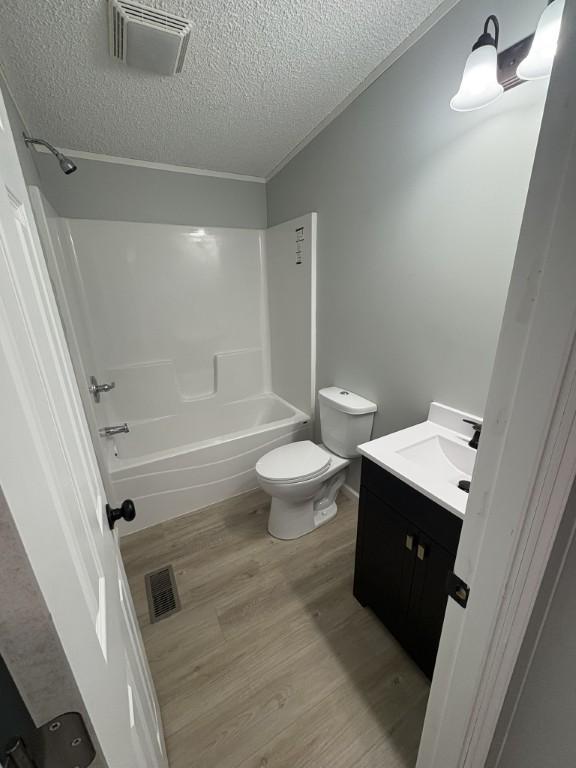 bathroom featuring a textured ceiling, washtub / shower combination, toilet, vanity, and wood finished floors