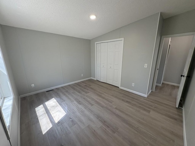 unfurnished bedroom featuring wood finished floors, lofted ceiling, a textured ceiling, a closet, and baseboards