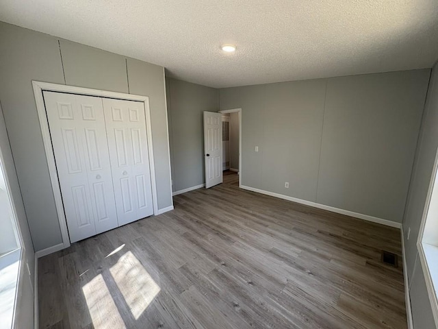 unfurnished bedroom featuring wood finished floors, a textured ceiling, baseboards, and a closet
