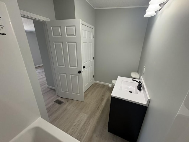 bathroom featuring wood finished floors, ornamental molding, vanity, toilet, and baseboards